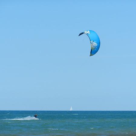 Persona fa kitesurf in mare con aquilone blu, cielo limpido.