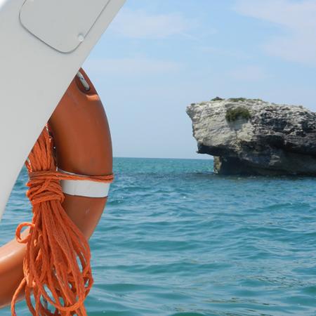 Salvagente arancione su barca, mare azzurro e scoglio sullo sfondo.