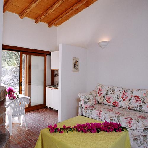 Salotto accogliente con divano floreale, camino e tavolo con tovaglia gialla e fiori.