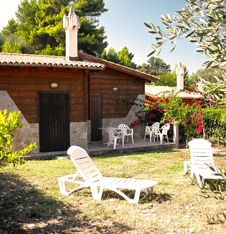Casetta in legno con giardino, sedie bianche e lettini prendisole.
